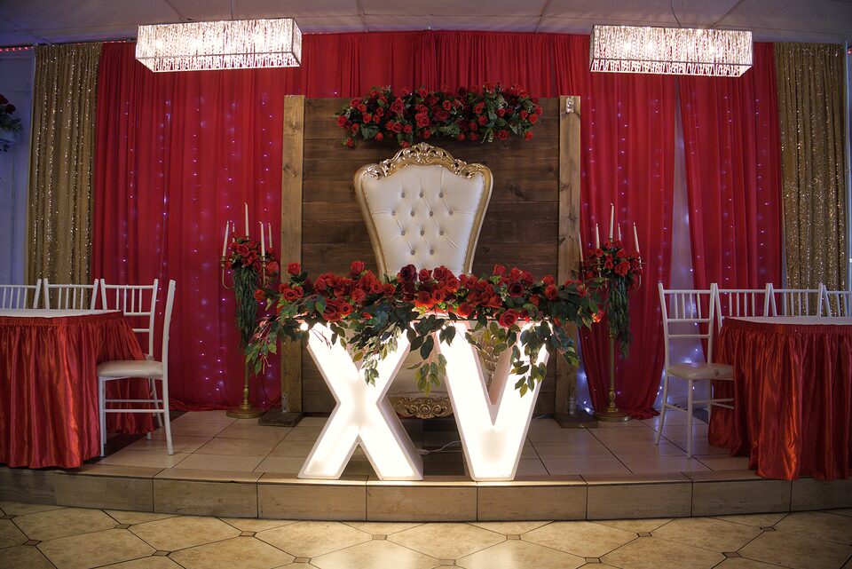 Escenario de quinceanera con trono dorado, rosas y letras XV iluminadas